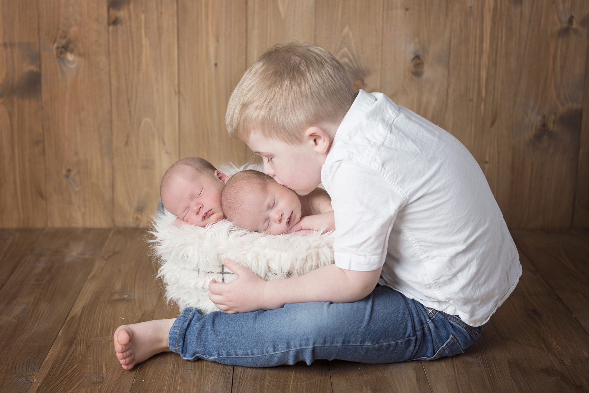 little boy kissing his newborn twin sisters in baby photography shoot Berkshire