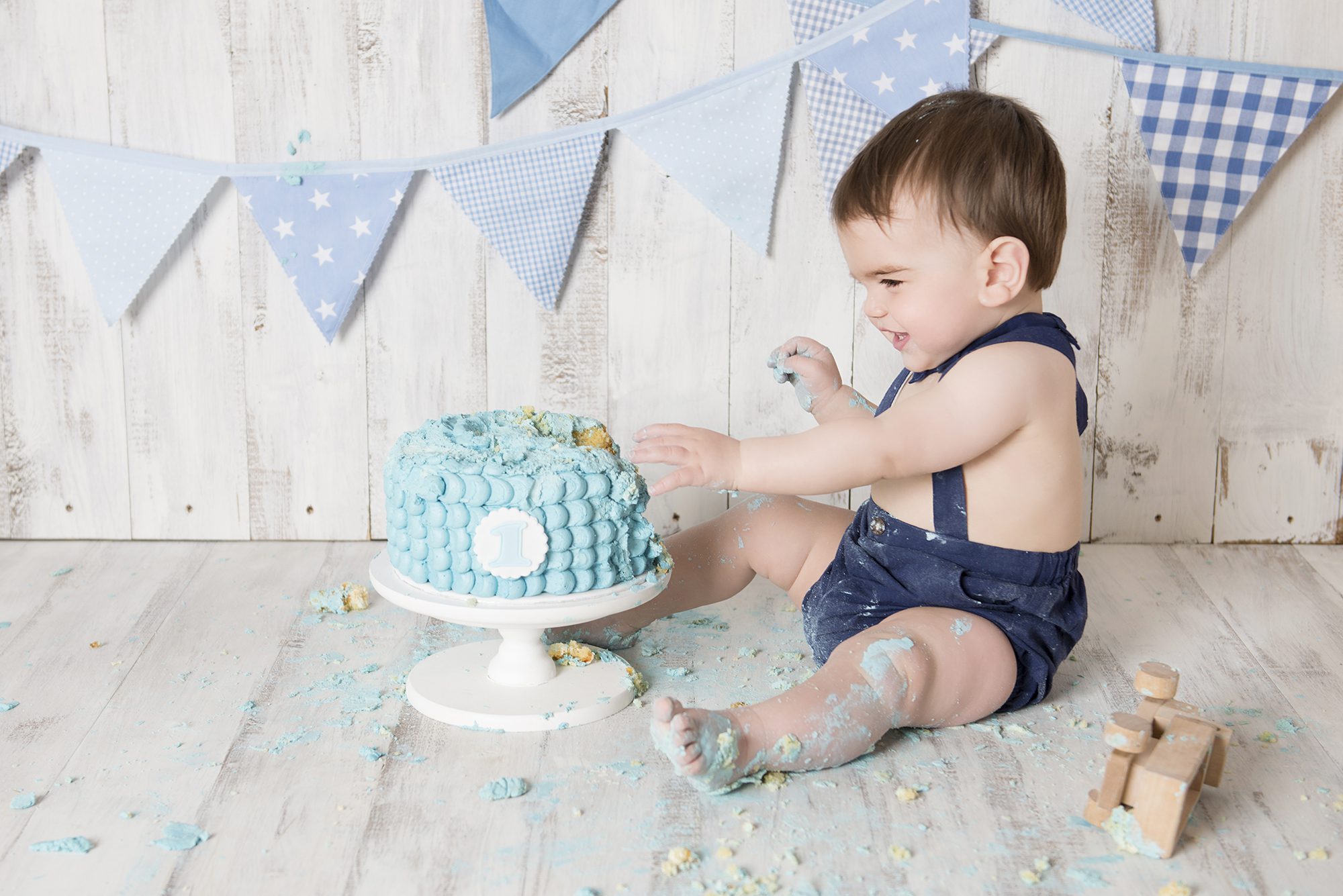 baby boy smashing blue cake for cake smash photos, reading